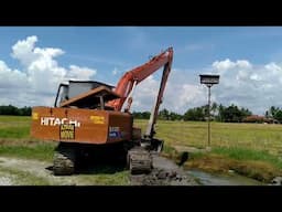 EXCAVATOR LONG ARM HITACHI EX120 MAKING A RIVER SLOPE NEAR PADDY FIELD